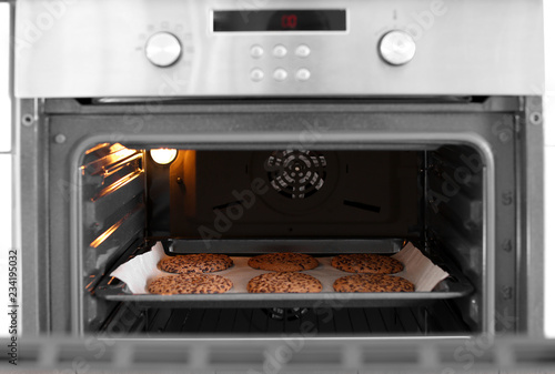 Open modern oven with freshly baked cookies on sheet in kitchen