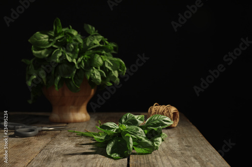 Fresh basil leaves on wooden table against black background. Space for text