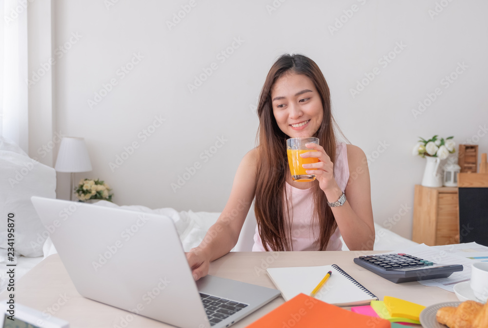 Asian female freelancer drink orange juice and and working on laptop at home.Work at home concept.work from home concept. Asian female freelancer drink orange juice and and working on laptop at home.Work at home concept.work from home concept.