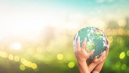 Child hands holding earth globe over green blurred city lights at sunrise background
