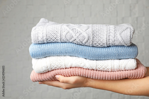 Woman holding stack of folded warm knitted sweaters against brick wall © New Africa