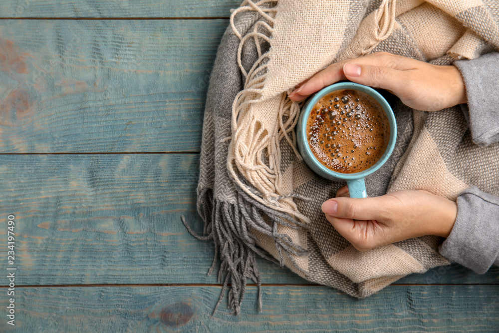 Woman with warm scarf holding cup of hot winter drink on wooden background, top view. Space for text - obrazy, fototapety, plakaty 