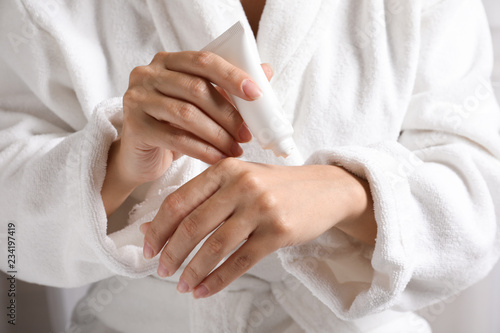 Woman in bathrobe applying moisturizing hand cream  closeup. Winter skin care cosmetic