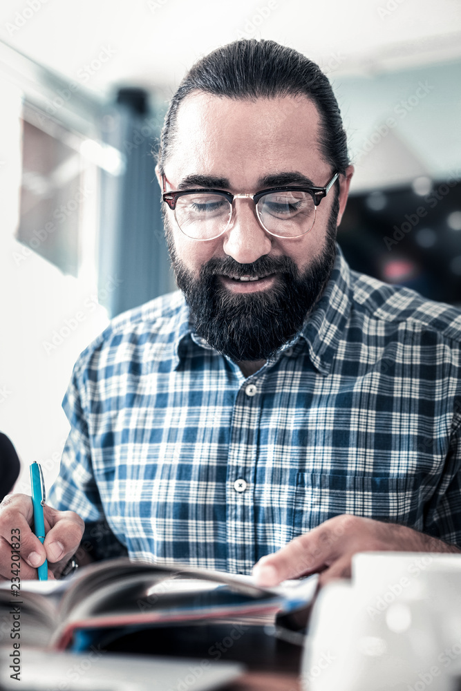Freelance writer. Dark-haired bearded professional freelance writer holding blue pen working hard Freelance writer. Dark-haired bearded professional freelance writer holding blue pen working hard