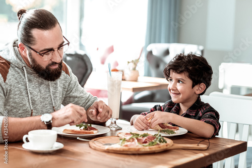 Yummy pizza. Bearded father and cute son eating extremely yummy pizza with bacon and cheese