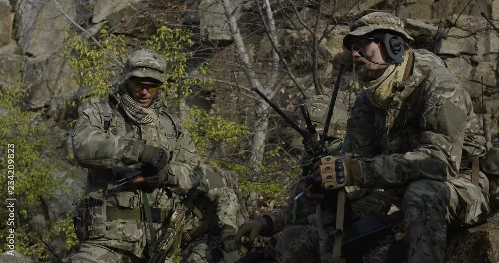 Medium slow motion shot of soldiers taking a break and checking a handgun while smoking Medium slow motion shot of soldiers taking a break and checking a handgun while smoking