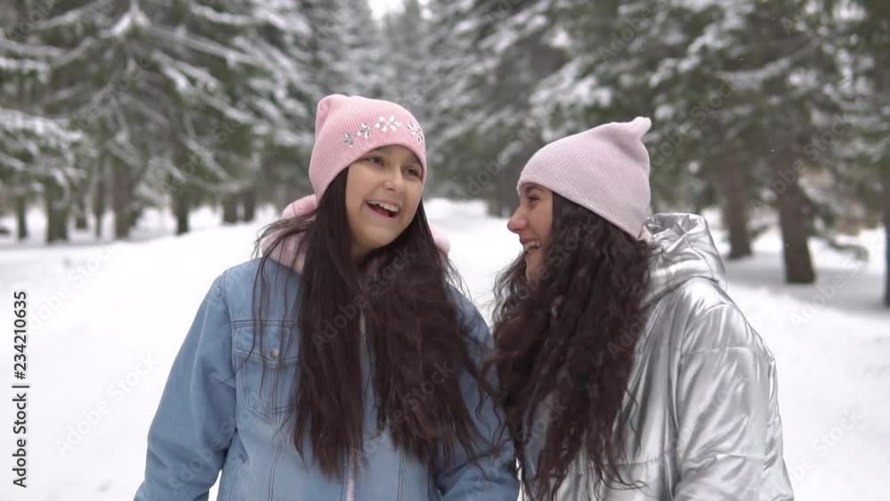 Two girlfriends in winter clothes and wearing a hat are walking in the woods in the winter having a good mood Two girlfriends in winter clothes and wearing a hat are walking in the woods in the winter having a good mood
