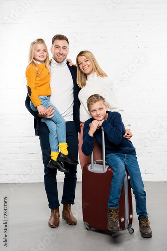 happy family ready to go on winter holidays with luggage looking at camera on white background