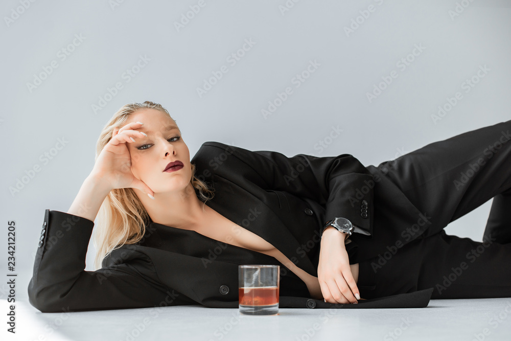beautiful stylish half naked woman in black trendy suit lying on grey with  glass of whiskey Photos