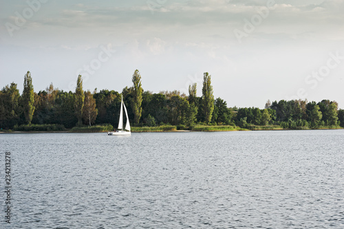 Sailing boat on a calm lake with reflection in the water. Serene scene landscape. Horizontal photograph.