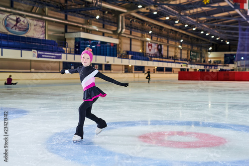 Full length portrait of little girl figure skating in indoor rink and looking at camera , copy space