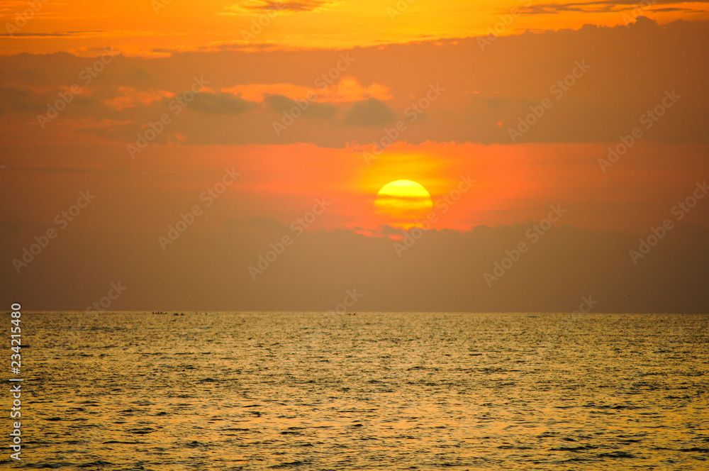 Cloudy orange sunset over sea. The orange sun is partially obscured by clouds