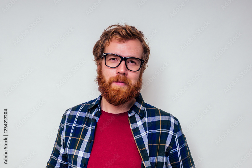 Close up portrait of redhead bearded male with red head and stylish glasses green tartan shirt and red cotton t-shirt on white background in studio. Close up portrait of redhead bearded male with red head and stylish glasses green tartan shirt and red cotton t-shirt on white background in studio.