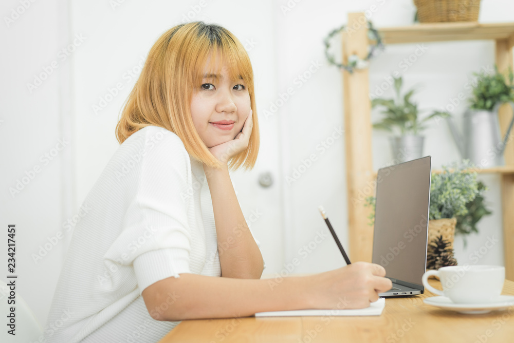 Beautiful young smiling asian woman working on laptop while sitting in a living room at home. Asian business woman working in her home office. Enjoying time at home. Beautiful young smiling asian woman working on laptop while sitting in a living room at home. Asian business woman working in her home office. Enjoying time at home.