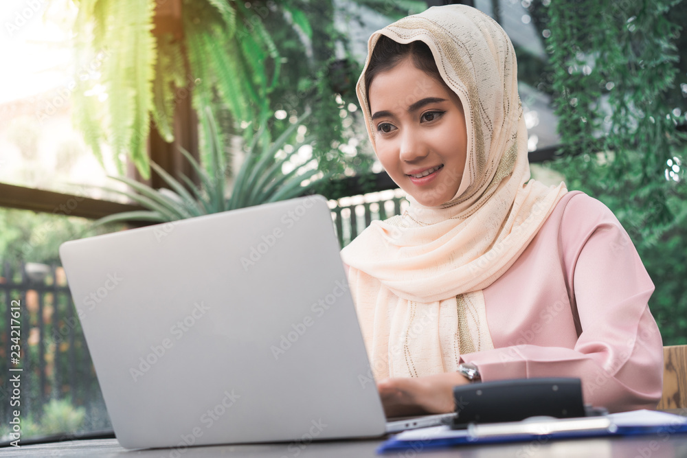 Beautiful young smiling asian muslim woman working on laptop sitting in living room at home. Asian business woman working document finance and calculator in her home office. Enjoying time at home. Beautiful young smiling asian muslim woman working on laptop sitting in living room at home. Asian business woman working document finance and calculator in her home office. Enjoying time at home.