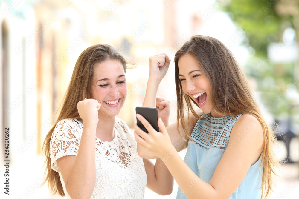 Excited friends checking online good news in a phone Excited friends checking online good news in a phone
