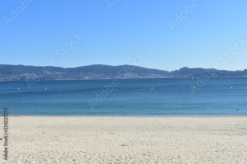 Beach with bright sand and clear water with turquoise and blue colours. Blue sky, sunny day. Galicia, Sanxexo, Rias Baixas, Spain. photo