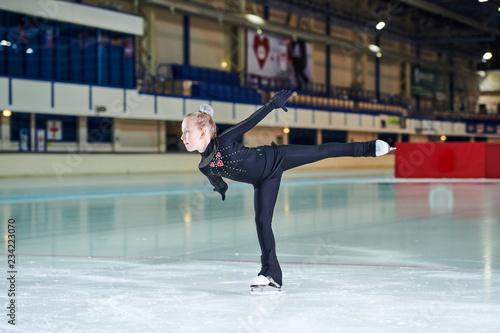 Full length portrait of little girl figure skating beautifully in indoor rink during competition or training, copy space
