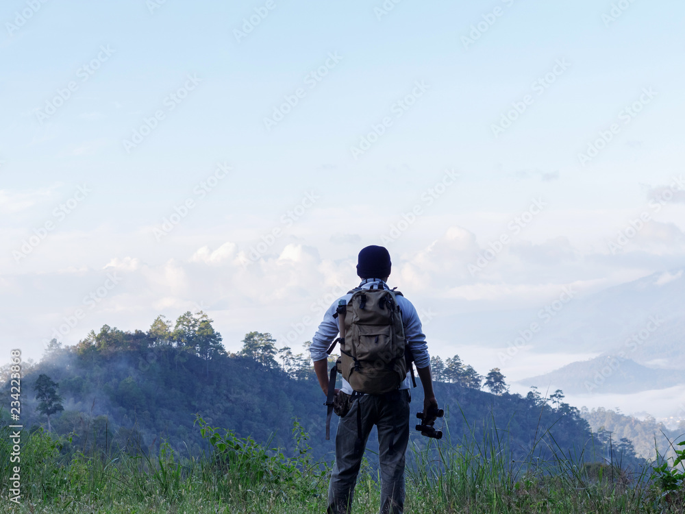 Young man with backpack and holding a binoculars standing on top of mountain Young man with backpack and holding a binoculars standing on top of mountain