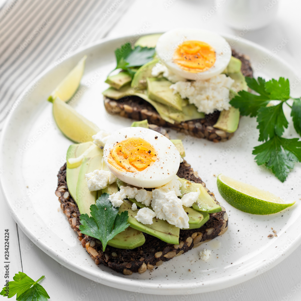 Toast with avocado, feta cheese and boiled egg on white plate, closeup view. Square crop. Avocado egg sandwich
