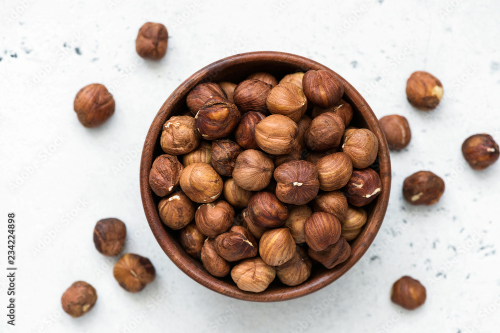 Fototapeta premium Hazelnuts in bowl. Unpeeled hazelnuts in wooden bowl on white background