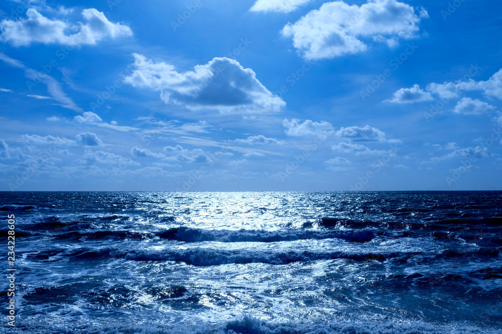 sea and sunlit blue sky with clouds the sunlit is glistening white off a deep blue sea