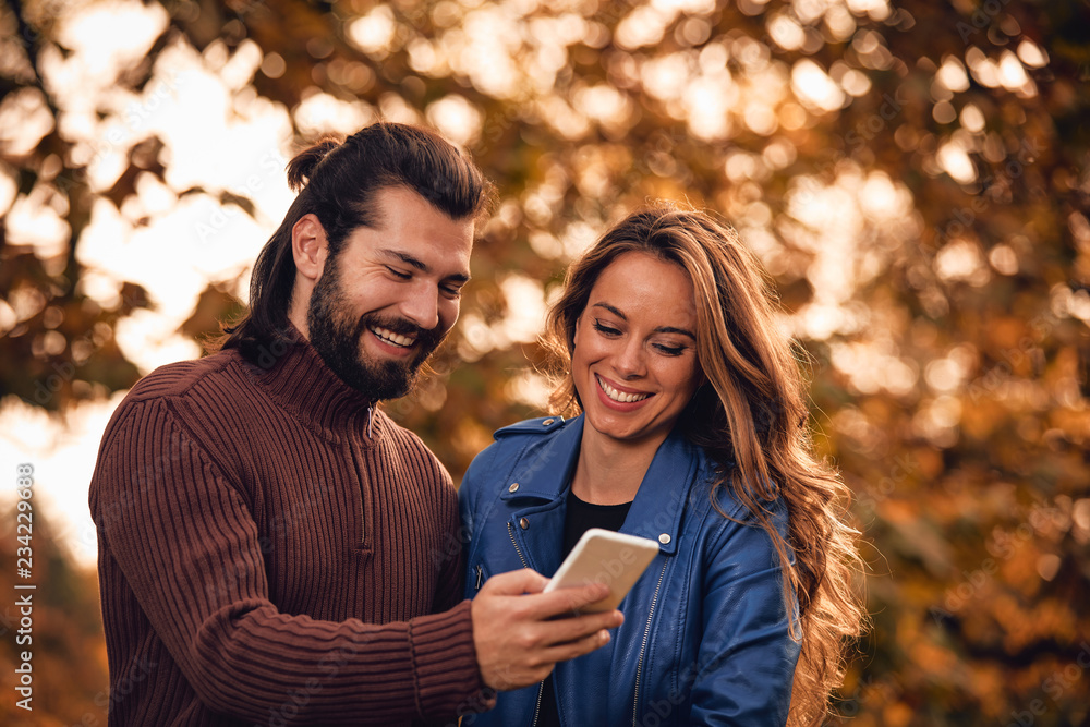 Young couple using cellphone in autumn colored park. Young couple using cellphone in autumn colored park.