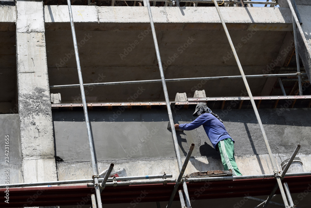 Filipino construction mason plastering grout on board scaffolding pipes on high-rise building alone