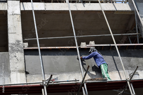 Filipino construction mason plastering grout on board scaffolding pipes on high-rise building alone