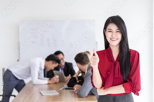 Asian young business girl thumbs up with office teamwork background.