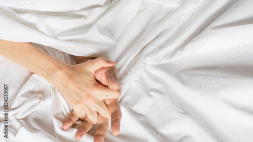 couples hold hands together in bed close-up touching each other on a white blanket.