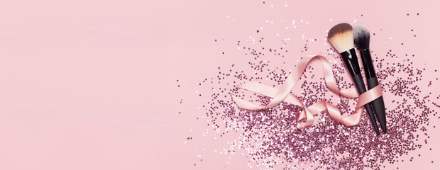 Two different Cosmetic makeup brushes with pink ribbon and holographic glitter confetti in the form of stars on pink background Flat lay top view copy space Makeup accessories holiday birthday newyear