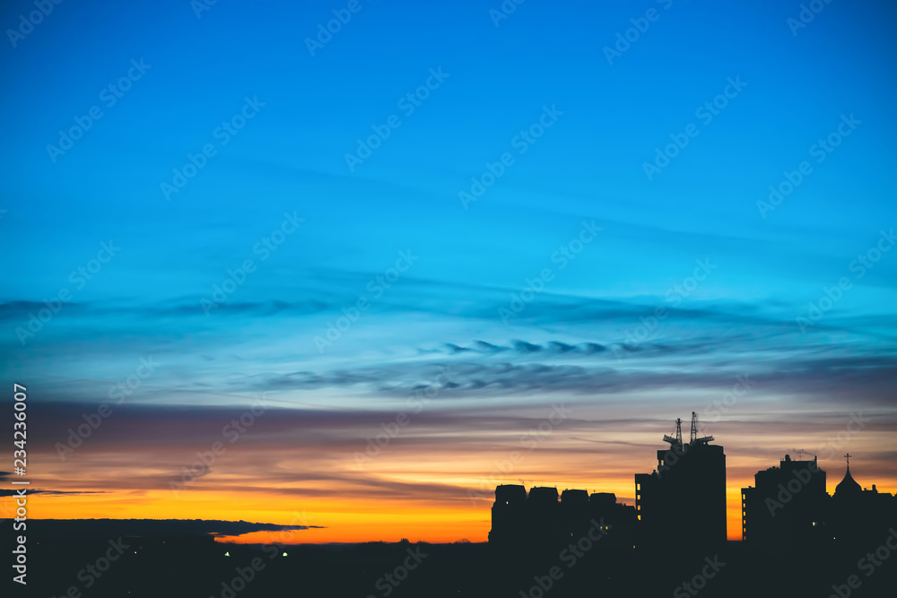 Cityscape with wonderful varicolored vivid dawn. Amazing dramatic blue sky with purple and violet clouds above dark silhouettes of city buildings. Atmospheric background of orange sunrise. Copy space.