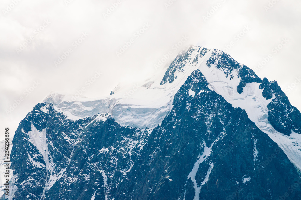Obraz premium Snowy mountain top in overcast sky. Rocky ridge in mist. Atmospheric minimalistic landscape of majestic nature.