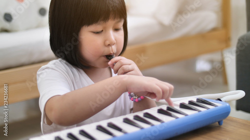 Happy little Asian girl playing melodica blow organ photo