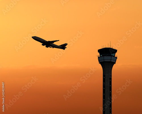 Air traffic control tower with a plane taking off at sunset