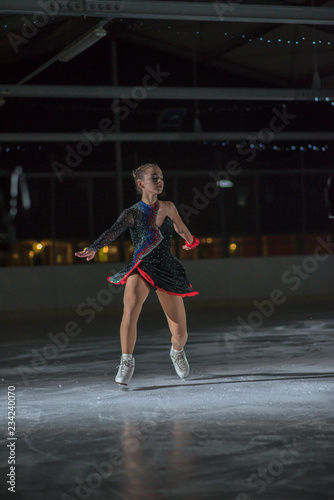 A young ice skater is holding her leg up in the air while she continues ice skating.