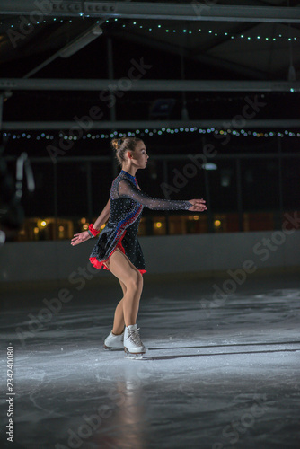 A young ice skater is slowly ice skating on the ice rink.