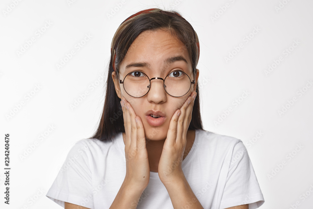 Studio shot of frustrated young Chinese female in round spectacles touching cheeks, having painful facial expression because of toothache. Nerdy Korean girl frowning, holding hands on face - obrazy, fototapety, plakaty 