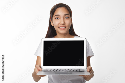 Cute Asian female saleswoman demonstrating new generic laptop computer with blank copyspace screen for your text or advertising content. Young Chinese woman posing in studio with electronic gadget