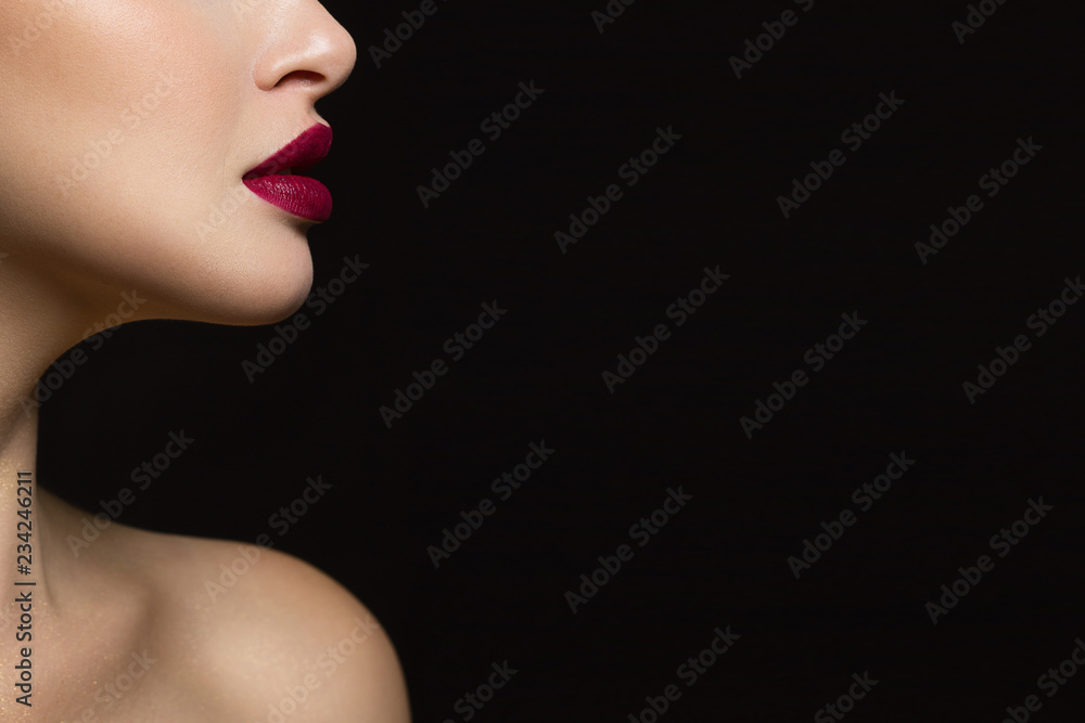Fototapeta premium Zbliżenie dolnej części twarzy kobiety o doskonałej skórze i pełnych ustach koloru marsala. Obraz na odosobnionym czarnym tle dodaje mu blasku.