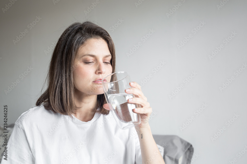 Beautiful charming woman drinking a big glass of water and wearing white clothes Beautiful charming woman drinking a big glass of water and wearing white clothes