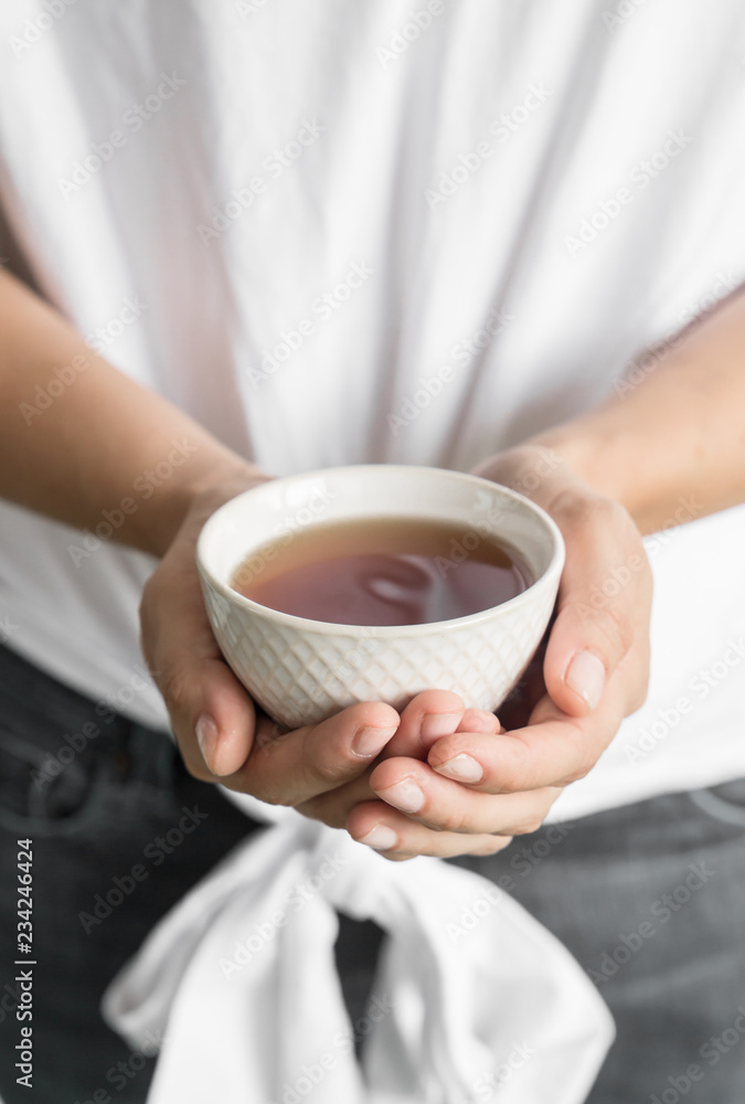 Nice and white cup of tea held up by woman's hands wearing white clothes Nice and white cup of tea held up by woman's hands wearing white clothes