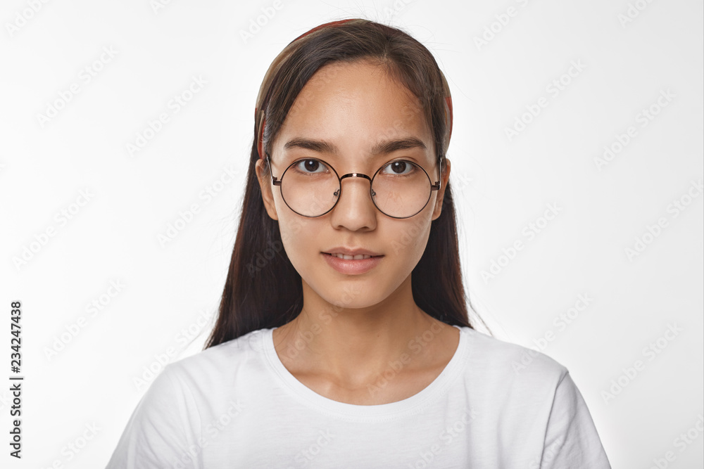 Horizontal image of cute Asian student girl wearing stylish round eyeglasses and white t-shirt posing isolated and smiling at camera. People, style, fashion, optics, vision and eyewear concept Horizontal image of cute Asian student girl wearing stylish round eyeglasses and white t-shirt posing isolated and smiling at camera. People, style, fashion, optics, vision and eyewear concept