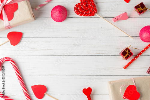 Valentines day background. Frame of red hearts, gift box with ribbon and candy sweets on a white wooden background, top view