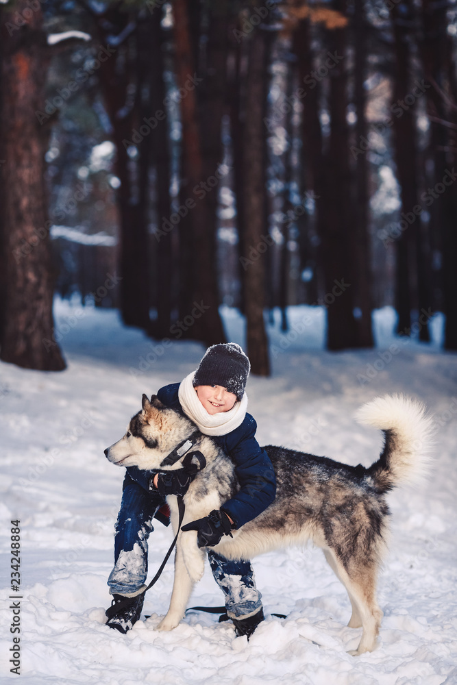 A cheerful European teenager hugs a big dog in the winter in the forest. The concept of winter holidays