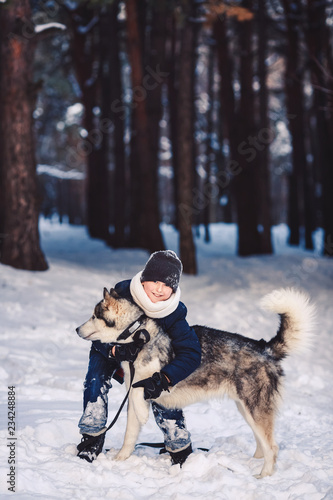 A cheerful European teenager hugs a big dog in the winter in the forest. The concept of winter holidays