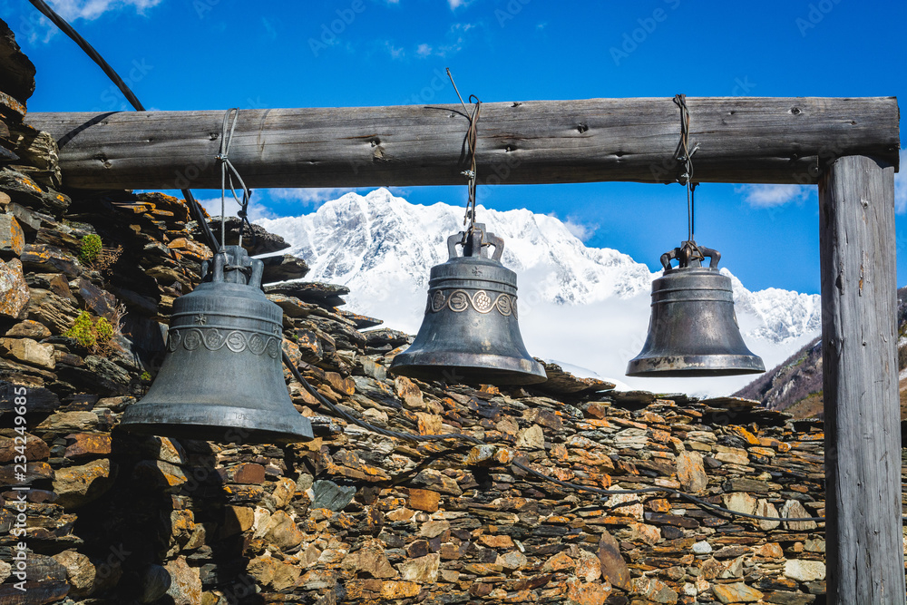 Obraz premium Bells in Lamaria church in Zhibiani - Ushguli community of villages, Upper Svaneti, Georgia. Snow covered peak of Shkhara mountain on background