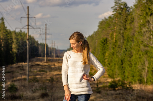 Woman in white knitted sweater posing against the backdrop of a forest clearing in the countryside