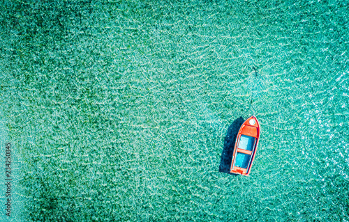 Aerial photo of a red lonely tboat tied up in crystal clear turquoise sea water